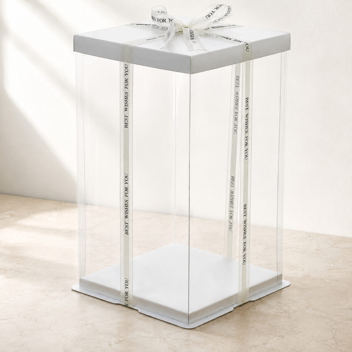 Tall empty clear cake box with a white square lid, white base and ivory printed ribbon