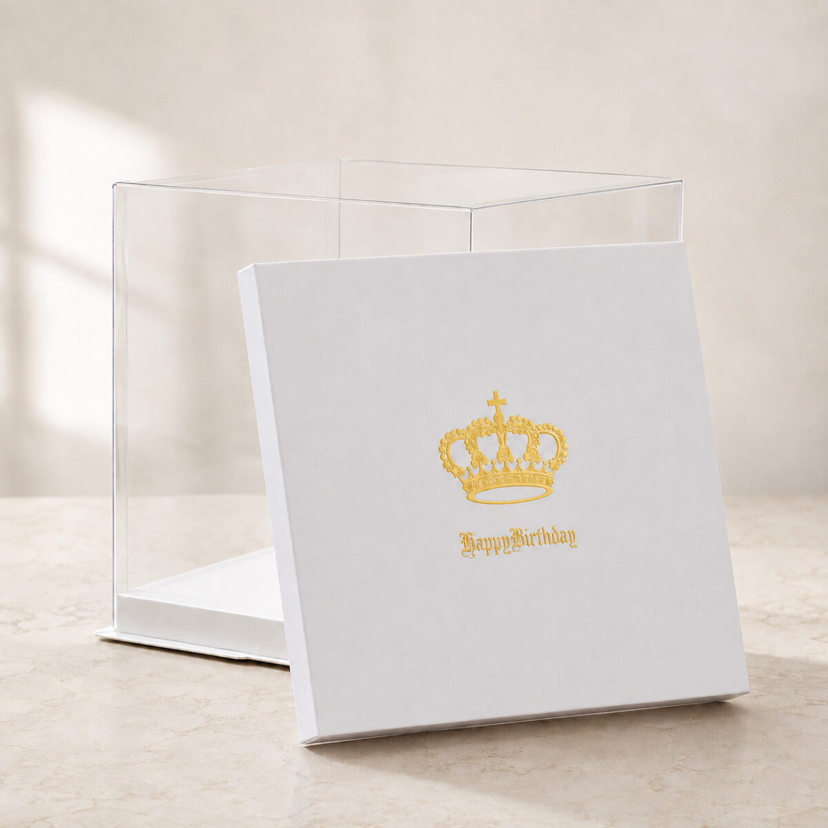 Empty clear square cake box with a white base and a detached white lid printed with a gold crown
