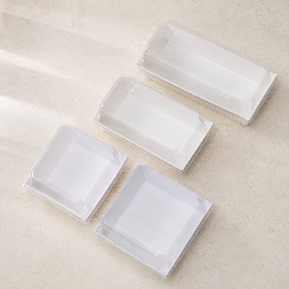 Four empty white packaging trays in two rectangular and two square formats with clear fitted covers