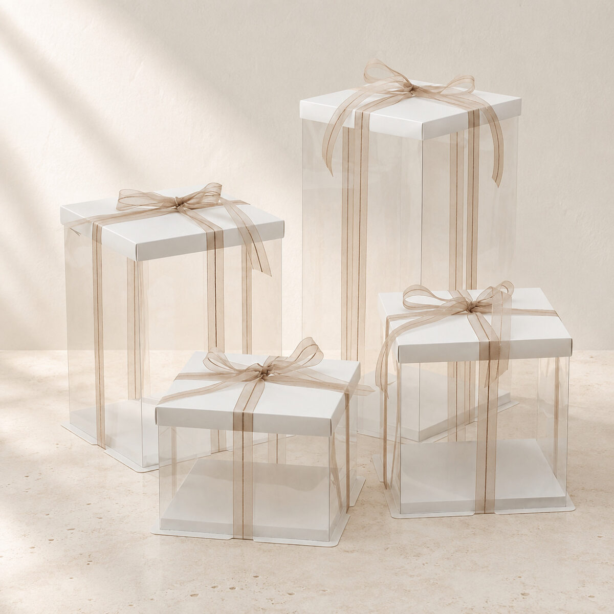 Square Clear Cake Boxes in Multiple Heights Four empty clear square cake boxes in different heights with white lids and gold beige ribbon bows