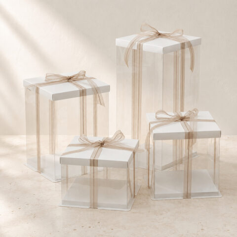 Four empty clear square cake boxes in different heights with white lids and gold beige ribbon bows