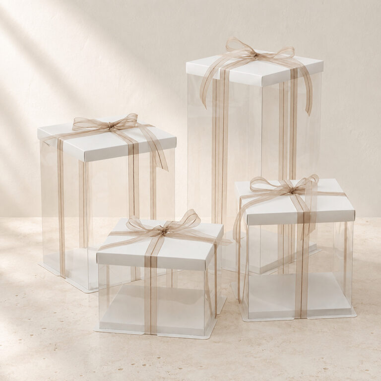 Four empty clear square cake boxes in different heights with white lids and gold beige ribbon bows