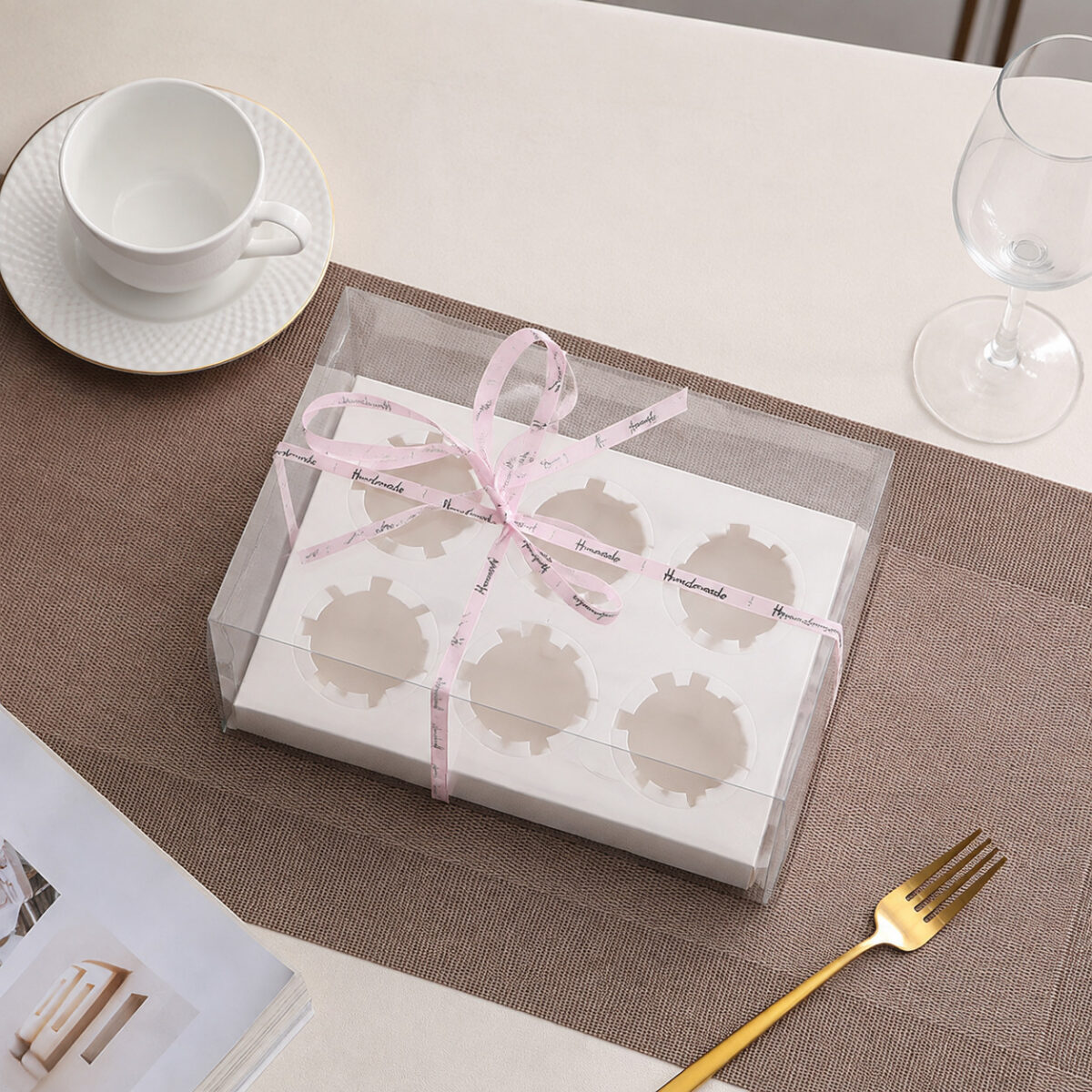 Clear Dessert Boxes with Cupcake Inserts Clear cupcake box with a white six-hole insert and pink Handmade ribbon on a woven placemat