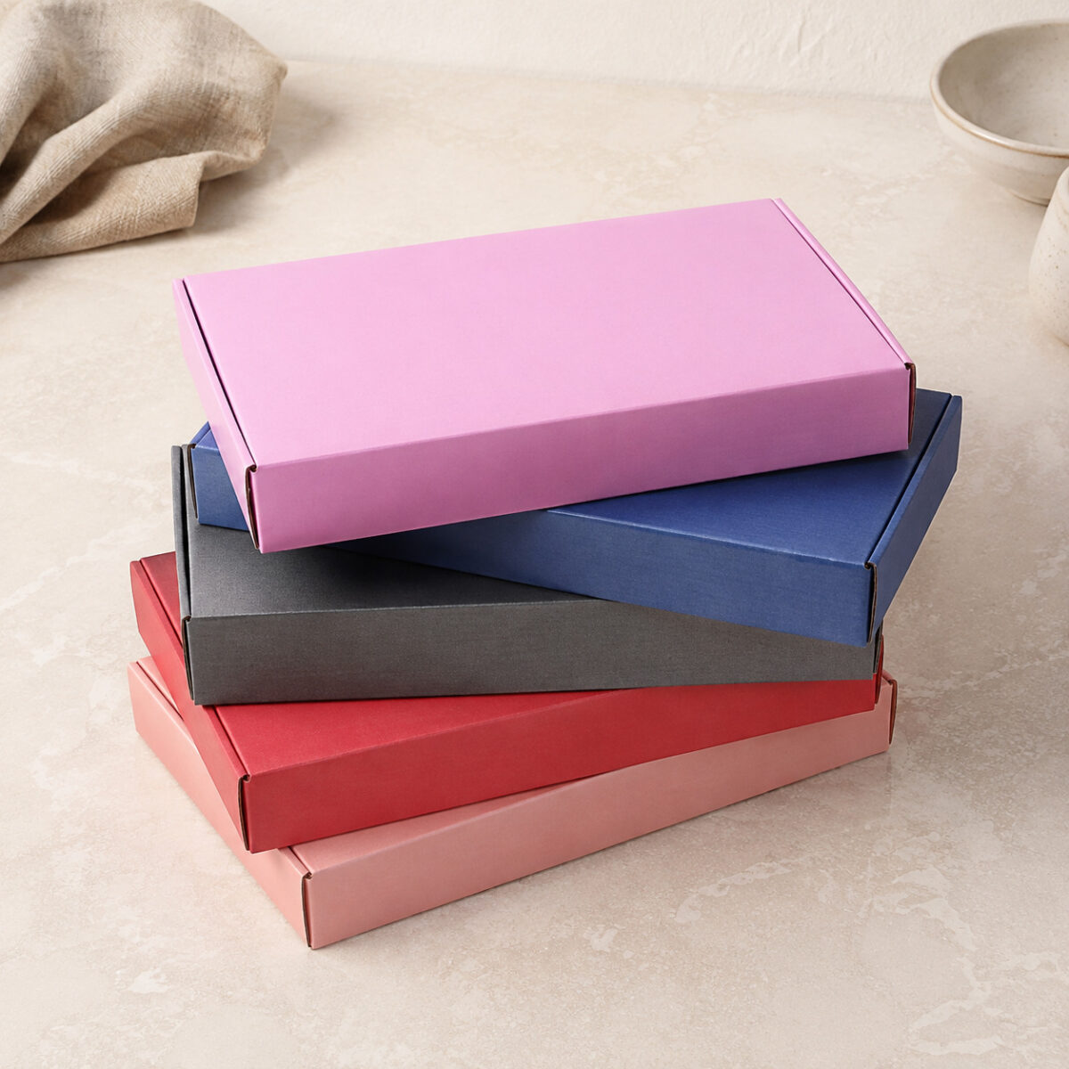 Design Gift Box Inserts Around Retention and Removal Five rectangular folding gift boxes stacked in pink blue charcoal red and peach on a pale counter