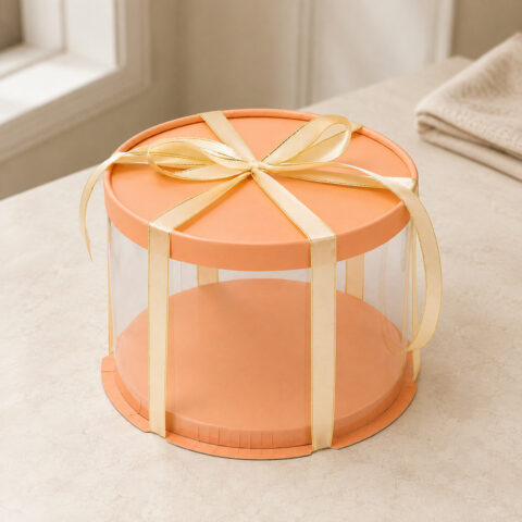 Clear round cake box with an orange lid and raised orange base tied with a gold-edged cream ribbon