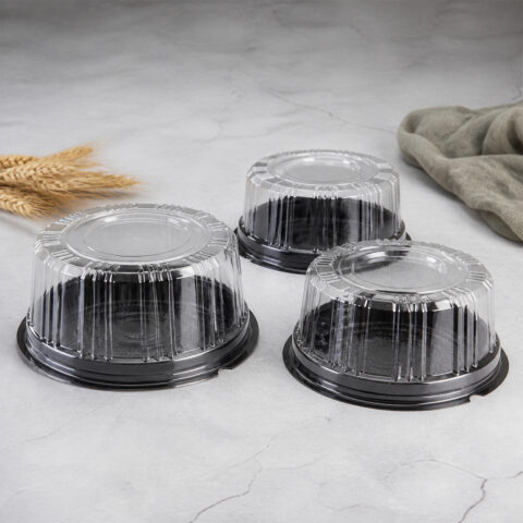 Mini Round Cake Containers with Black Bases Three clear ribbed mini cake containers with black round bases on a pale stone counter