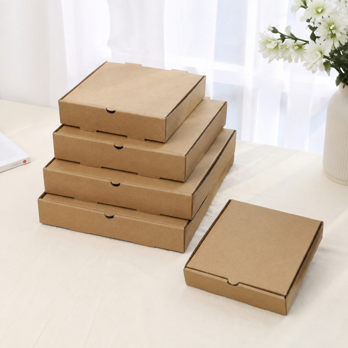 Plain Brown Kraft Pizza Boxes Five plain brown kraft pizza boxes in graduated sizes on a light tabletop