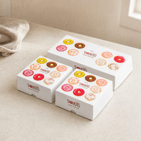 Two square and one rectangular white doughnut cartons with colorful doughnut artwork and front thumb notches