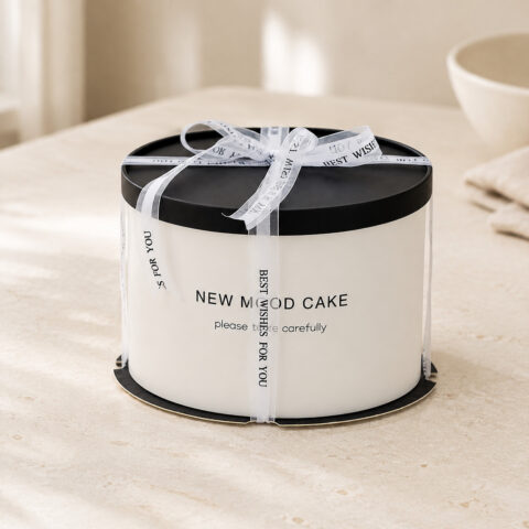 Round white paper cake box with a black lid and base, transparent outer sleeve and Best Wishes for You ribbon