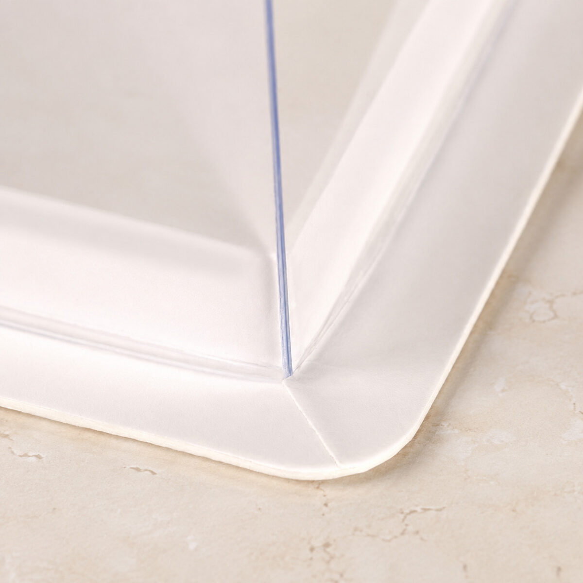 Close-up of a clear cake box corner meeting a white folded base and rounded outer flange