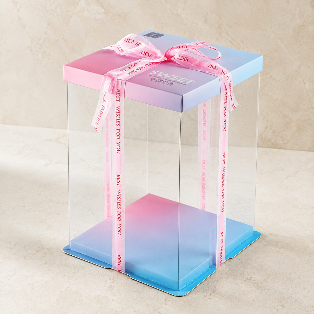 Tall clear square cake box with a pink and blue gradient lid and base and Best Wishes for You ribbon