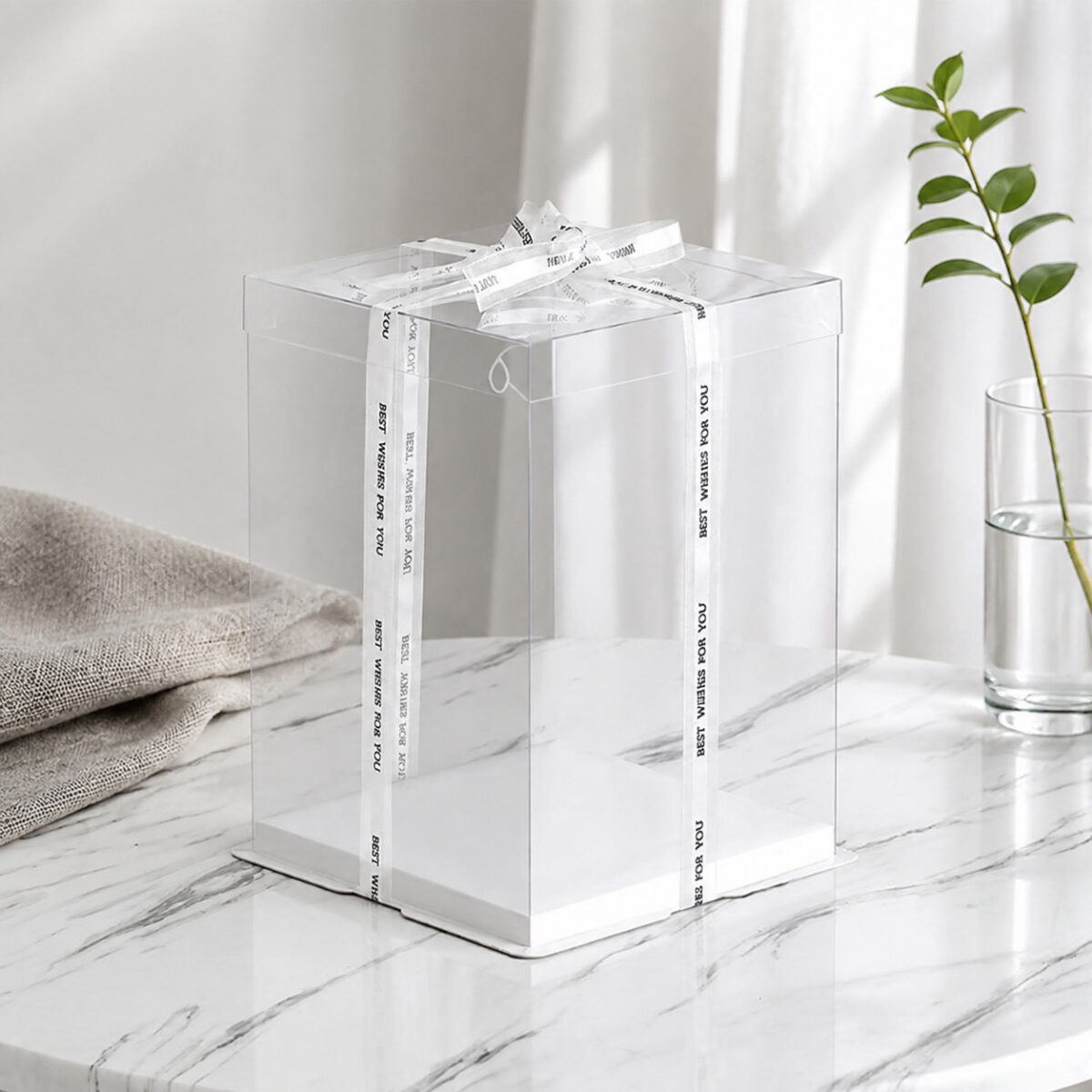 Tall transparent square cake display box with a white base and Best Wishes for You ribbon