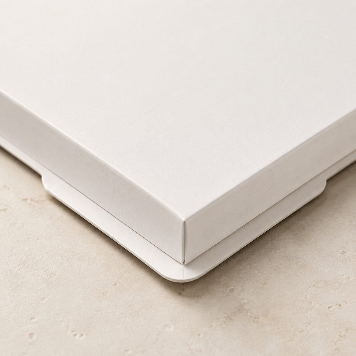 Close-up of a folded white cake box base corner, thin rounded flange and side notch