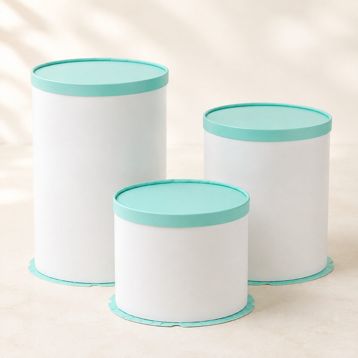 Three white cylindrical cake boxes in different heights with solid mint green lids and matching bases