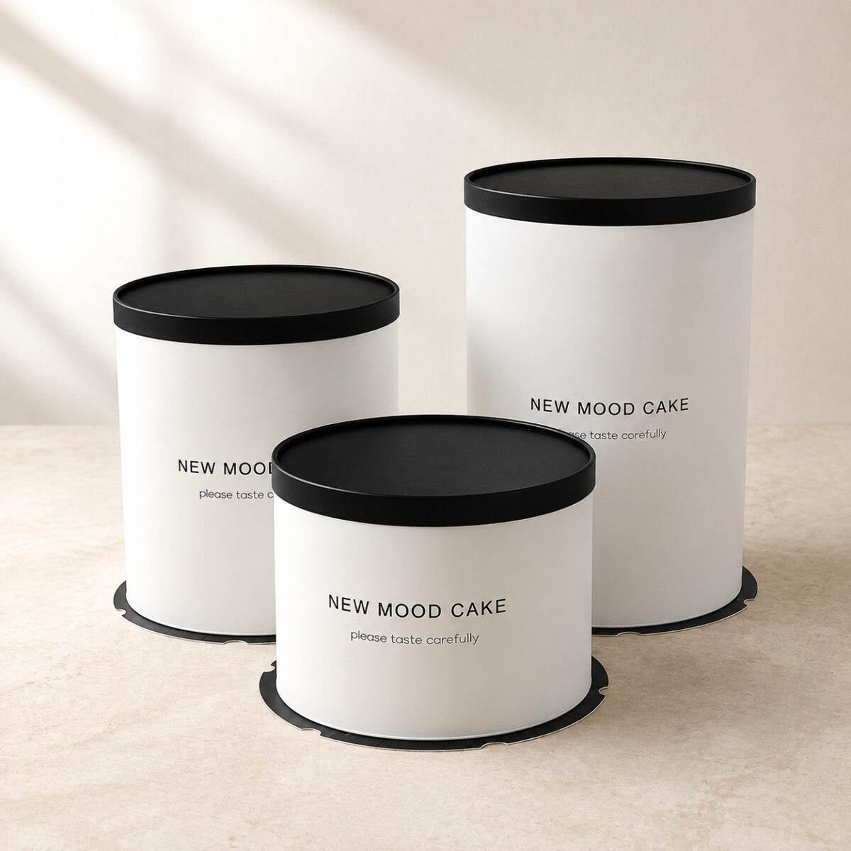 Three white cylindrical cake boxes with solid black lids, black bases and New Mood Cake printing