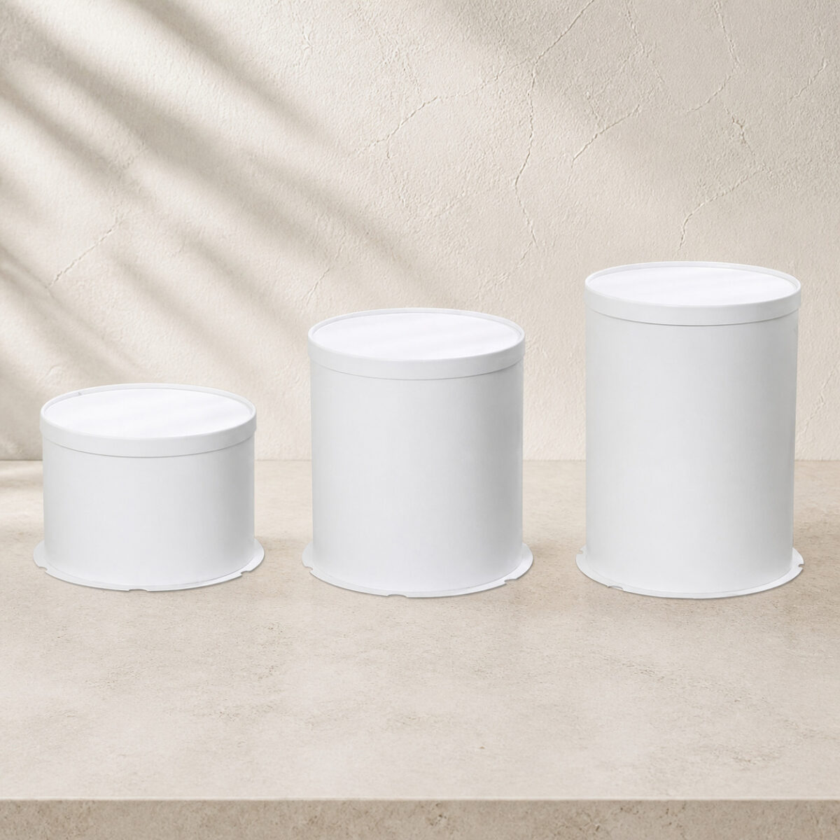 Three plain white cylindrical cake boxes shown from low to tall on a shared tabletop