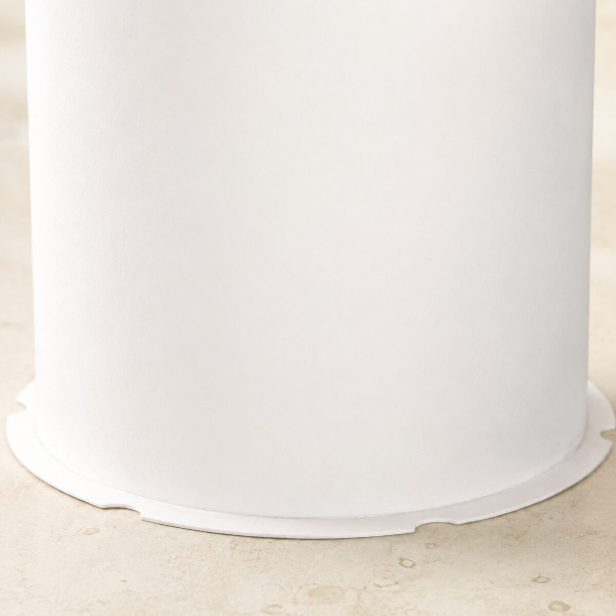 Close-up of a white cylindrical cake box wall and its thin notched circular base flange