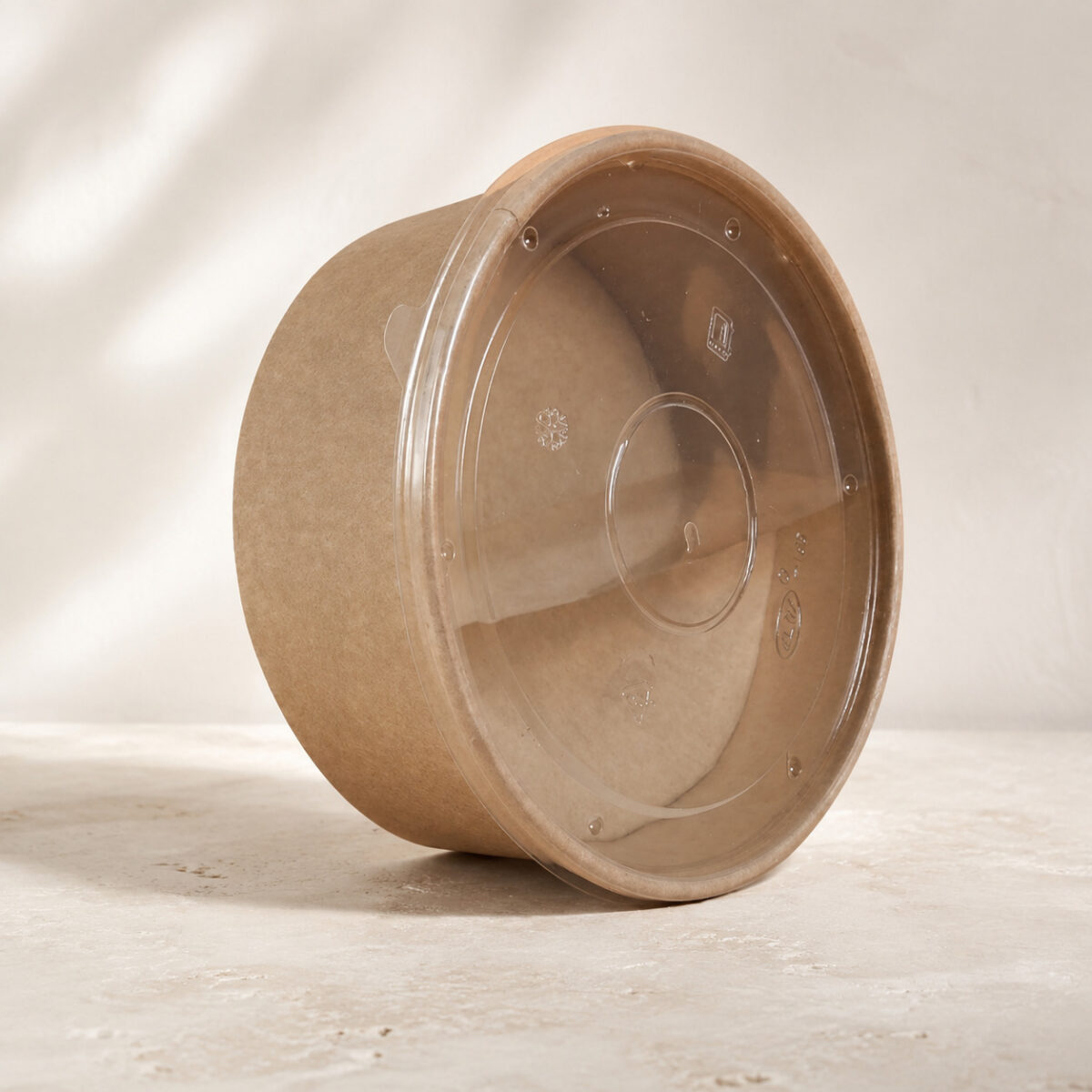 Kraft paper food bowl tilted on its side with a transparent molded lid attached